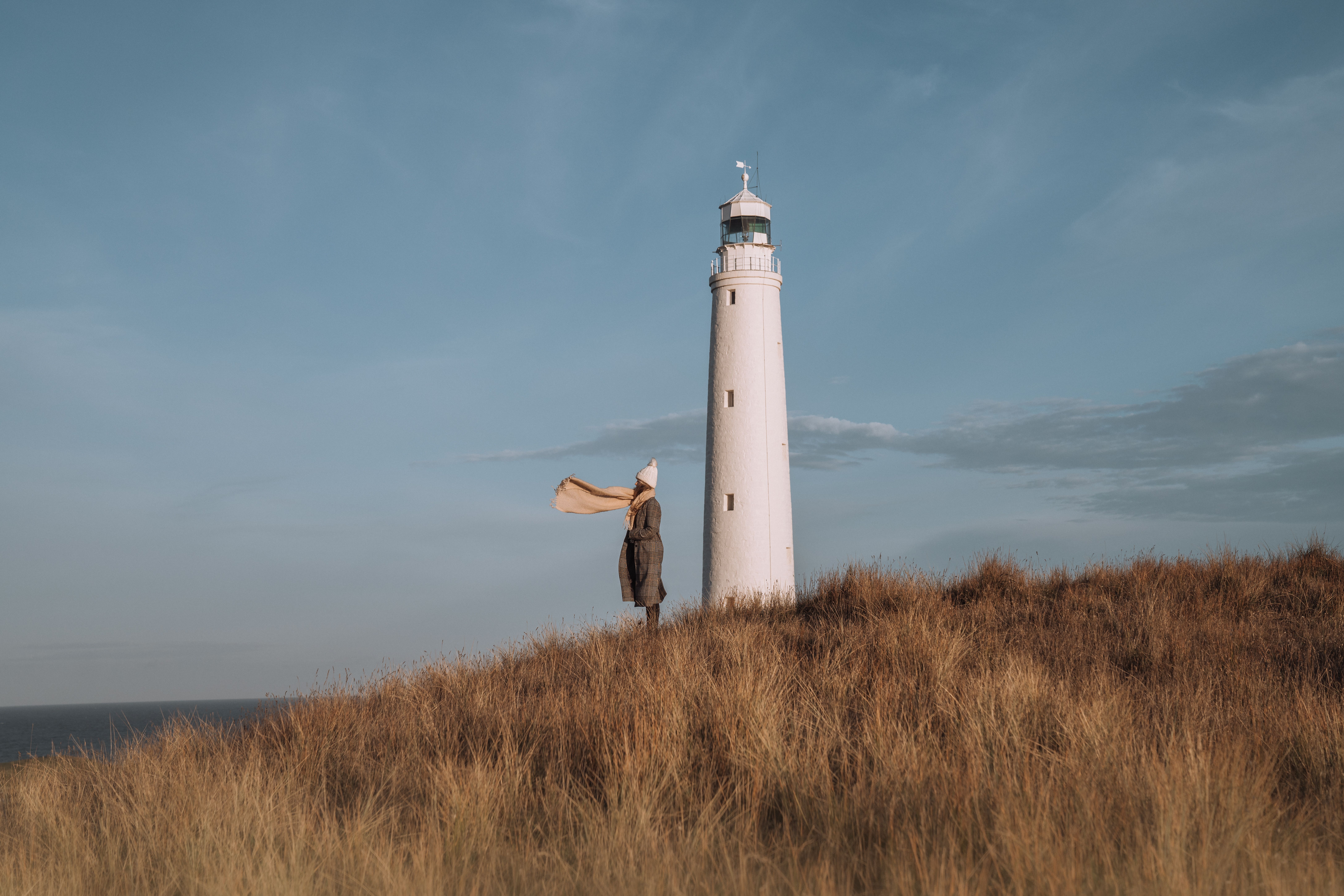 A person with a scarf blowing in the wind standing beside Cape Wickham Lighthouse, King Island, Tasmania