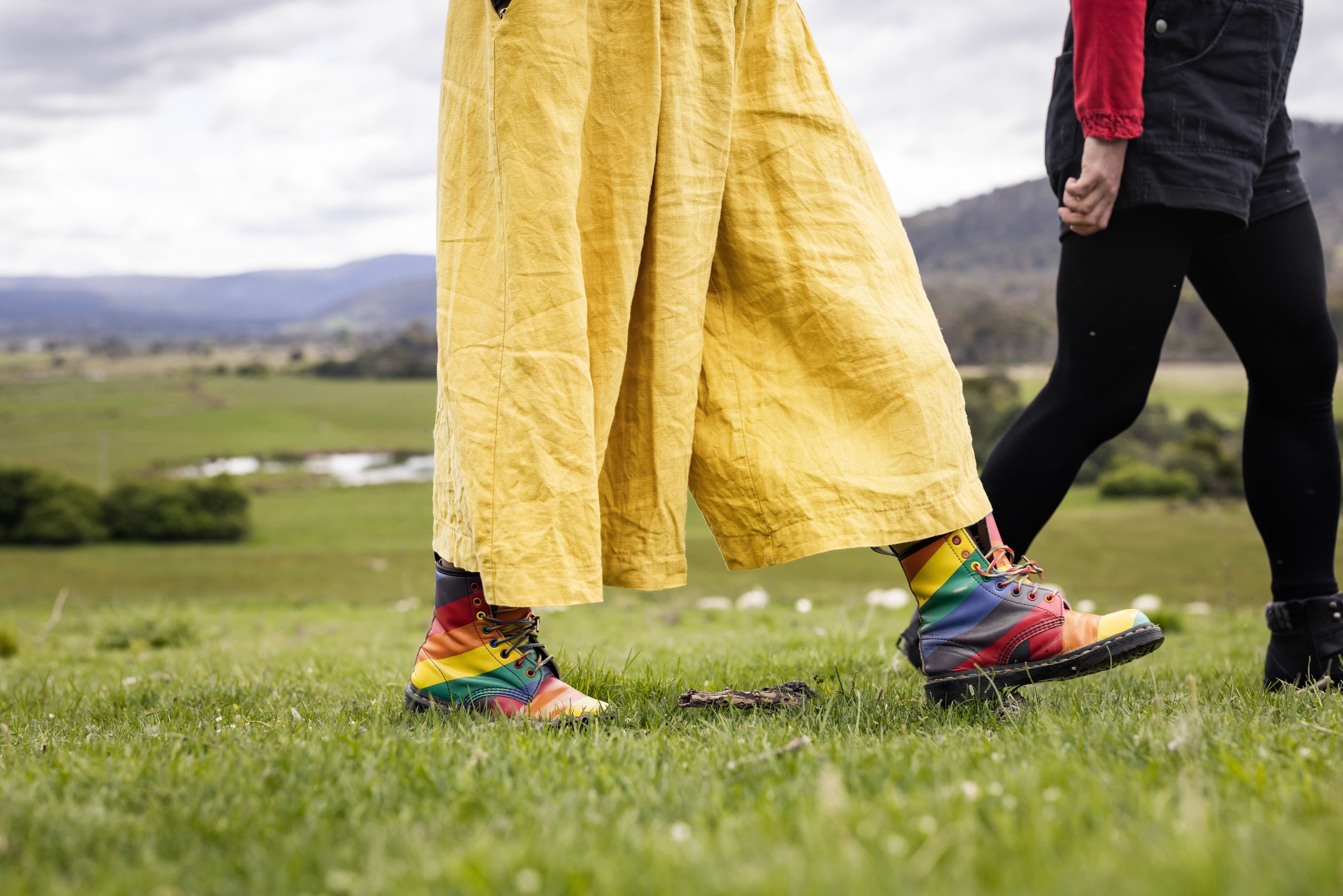 Two people walking on green grass at Twamley Farm, Buckland, one wearing rainbow boots and yellow trousers