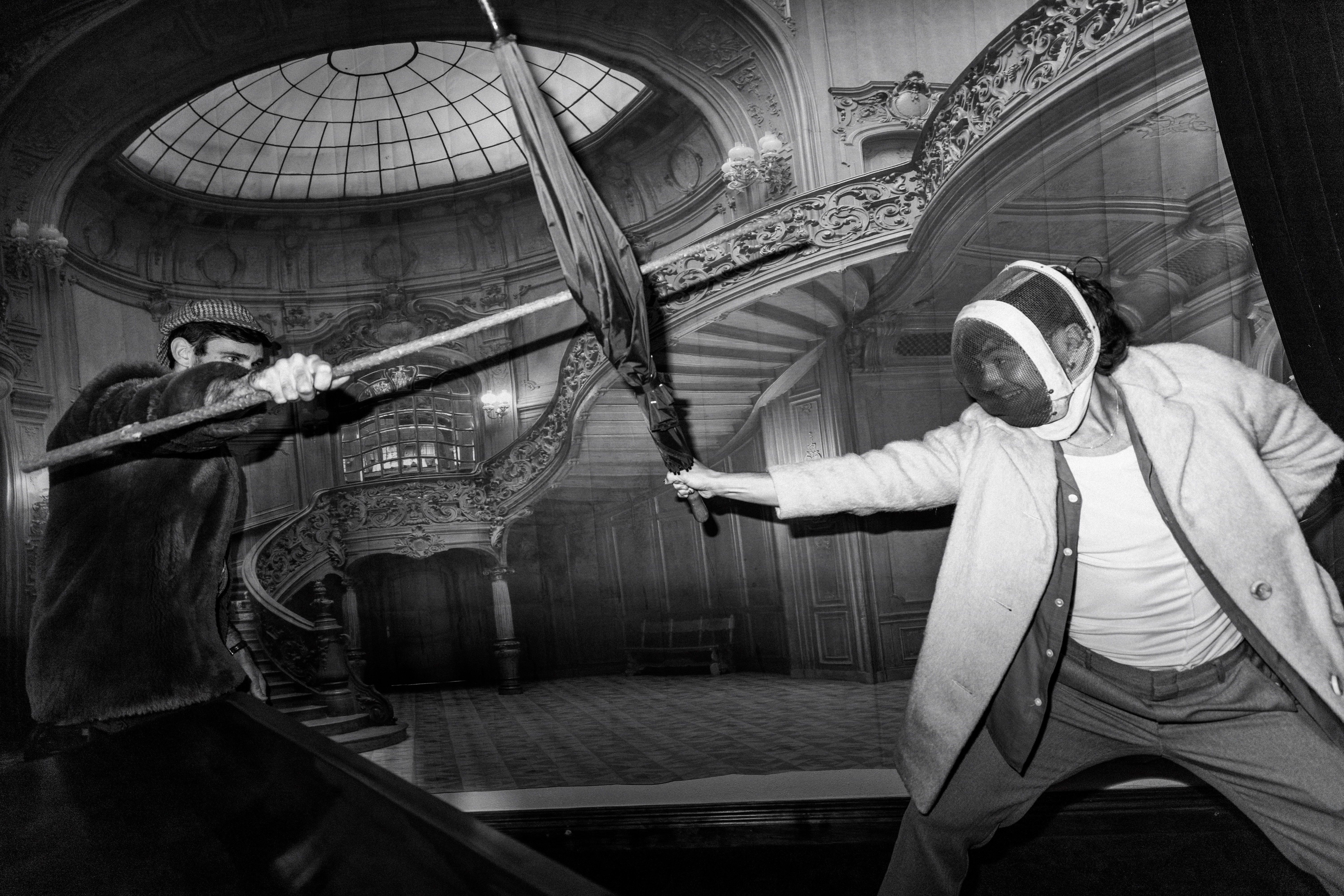 Black and white image of two people fencing with umbrellas in an ornate interior at The Secret Bank Society, Ringarooma