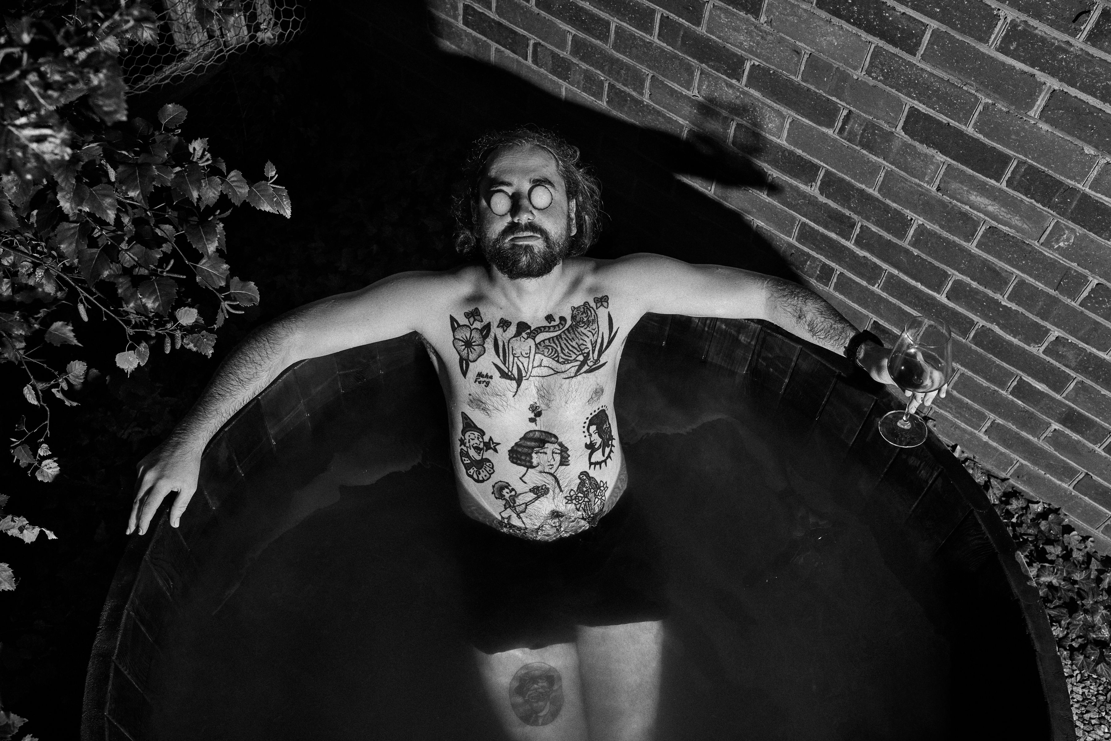 Black and white overhead shot of a person relaxing in an outdoor bath holding a glass of wine at Twamley Farm in Buckland