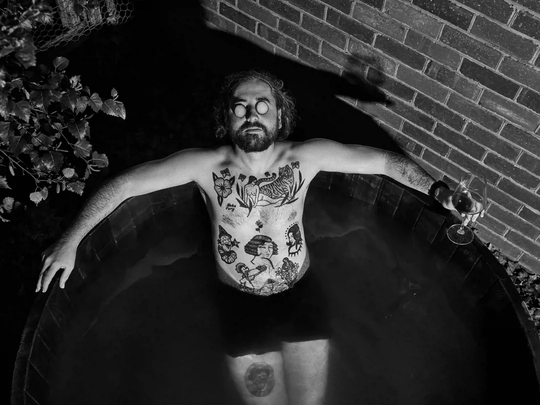 Black and white overhead shot of a person relaxing in an outdoor bath holding a glass of wine at Twamley Farm in Buckland