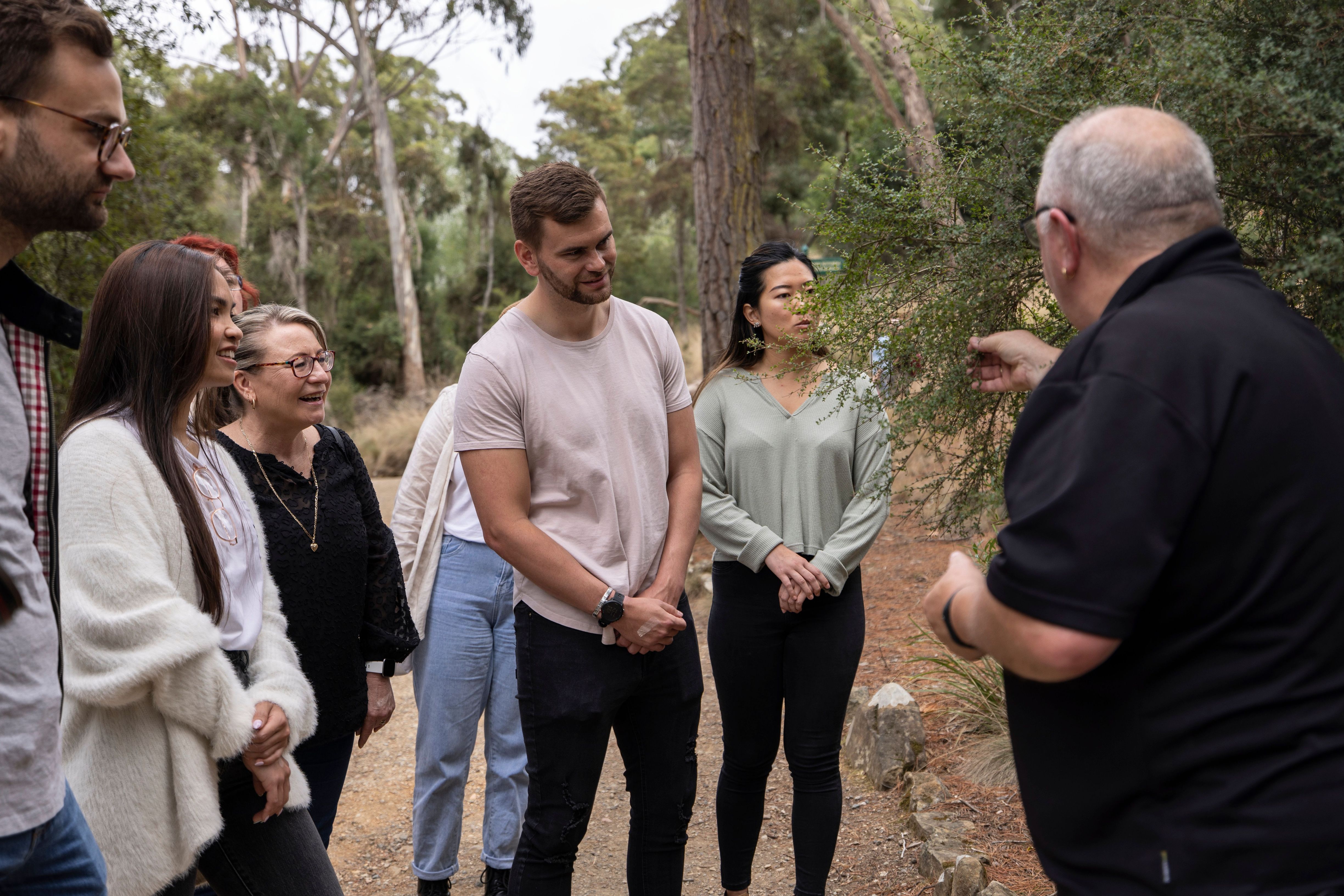 Visitors listen as a guide speaks and gestures on a bushland trail during a kooparoona niara Tours experience in Launceston