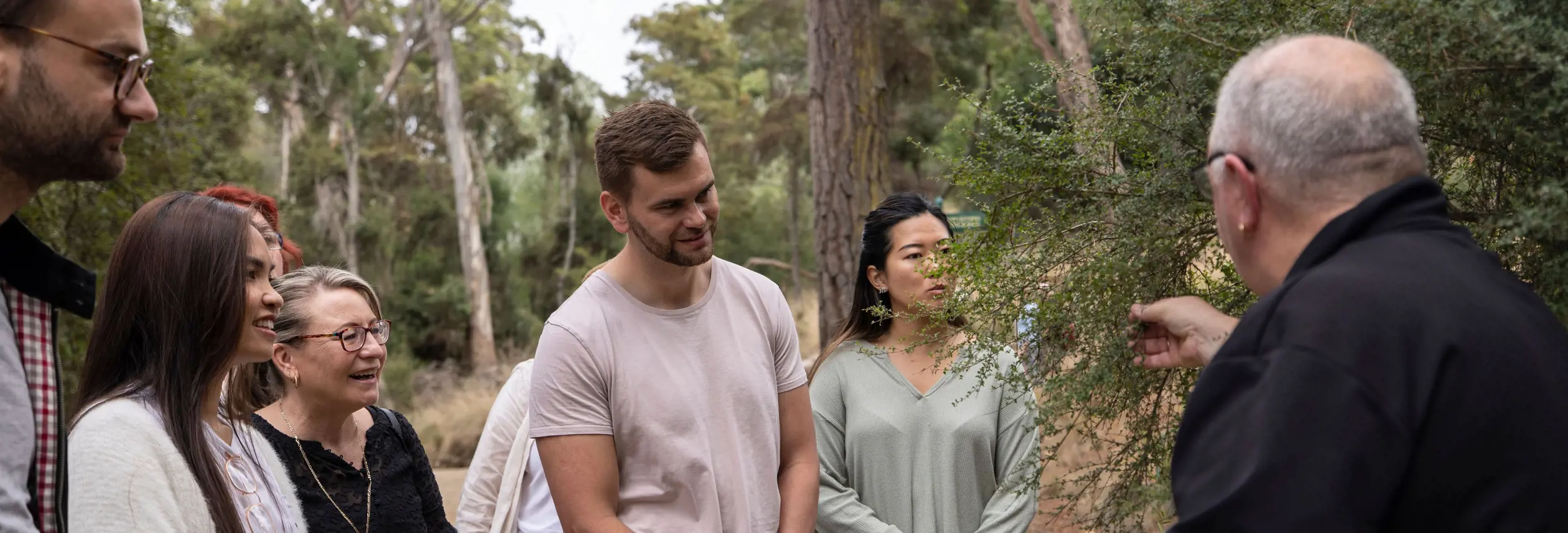 Visitors listen as a guide speaks and gestures on a bushland trail during a kooparoona niara Tours experience in Launceston