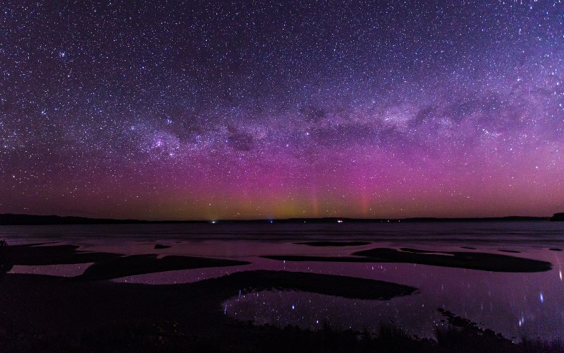 Hues of orange, pink and purple light the low horizon on a dark starry night in Tasmania.