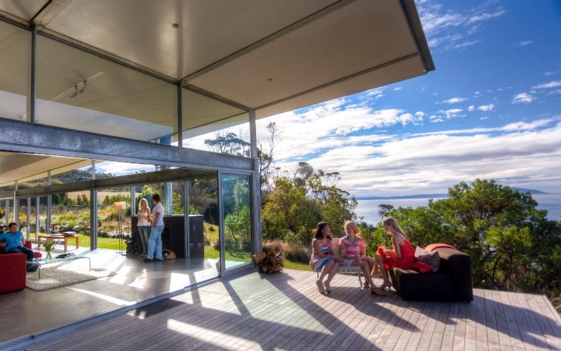 A group of women sit on outdoor furniture on a large deck in the shade of the modern architectural awnings of Avalon Coastal Retreat 