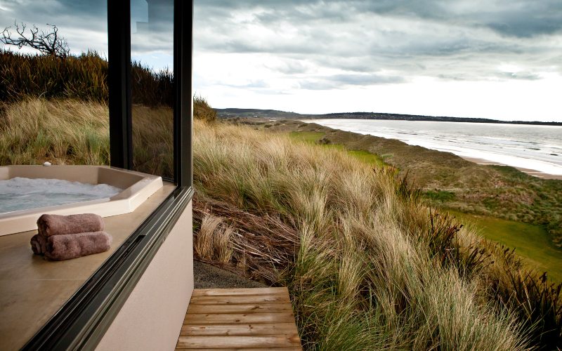 A indoor sauna with large windows looks out over the grassy hills to the beach on a cool day in the north east of Tasmania