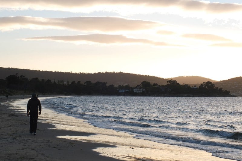 A man walks along the sand at Bellerive Beach at twilight.