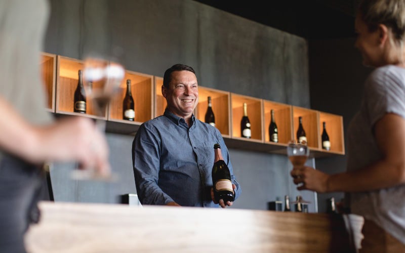 A man holding a bottle of Clover Hill, conducting wine tastings with a customer