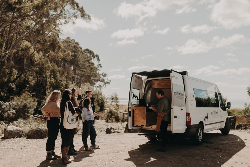 A group of young people watch as a chef prepares fresh food for them from his mobile kitchen.