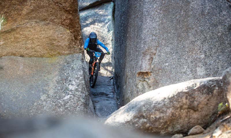 A professional mountain bike rider squeezes his bike through a narrow gap between two granite boulders