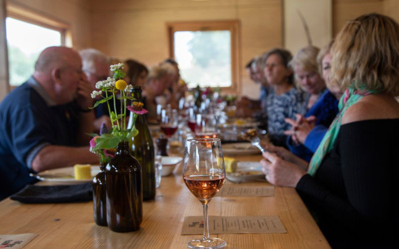 A full class of people sit at a long table eating meals prepared during cooking lessons at the Fat Pig Farm