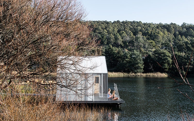 Two women sit on the deck of the sauna's floating platform, overlooking Lake Derby