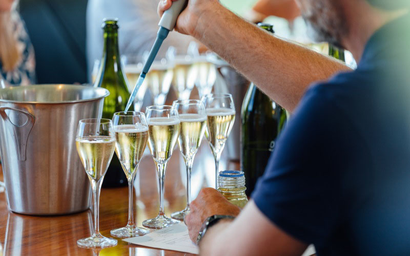 Man using a pipette  filled with a liqueur solution to create 5 varieties of sparkling wine 