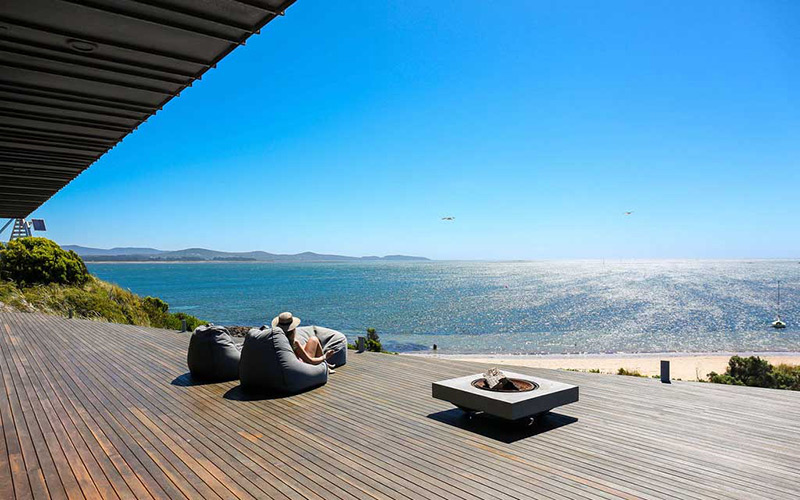 A lady sits on a beanbag on a wood deck looking at the beach