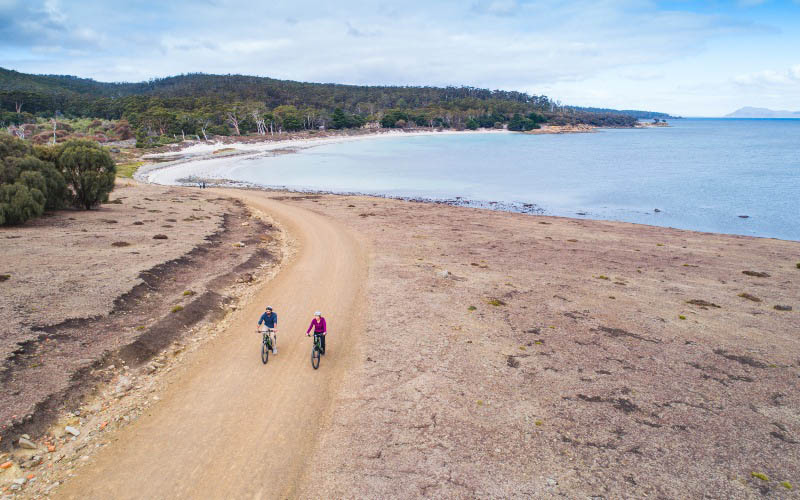 Two cyclists ride on a coastal gravel path on Maria Island, Tasmania