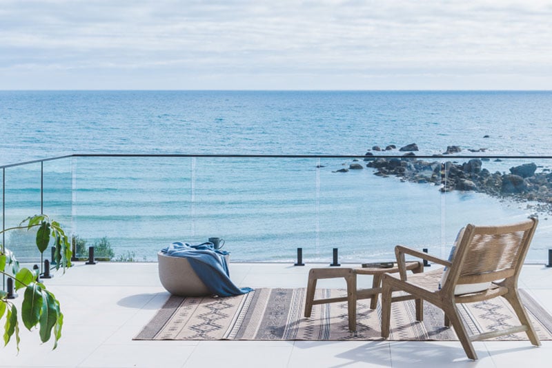 A mid-century Scandinavian style wooden chair overlook the sea on a raised verandah