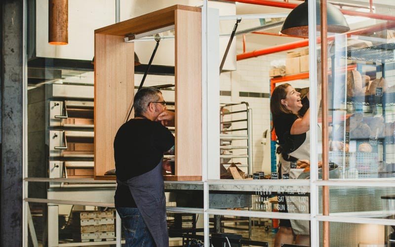 A man and a woman laugh while they work in the kitchen at Pigeon Whole Bakers