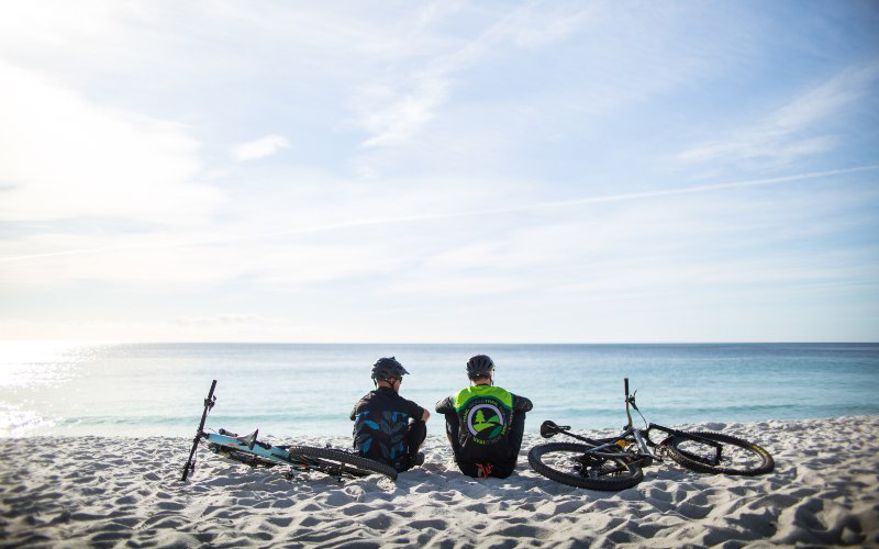 Two mountain bike riders rest on the white sands of a beach near St Helens, Tasmania.