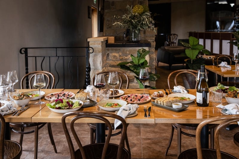A tastefully decorated and moodily lit room featuring a long wooden table with generous servings of bread, antipasto and wine.