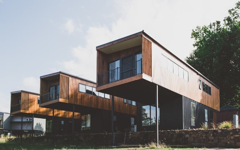 Three cantilevered cabins made of wood, extend outwards over a stone wall