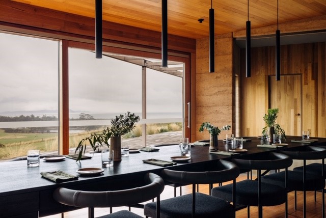 A photo of a contemporary interior with wooden panel walls, black leather chairs, a sleek table and suspended lighting.